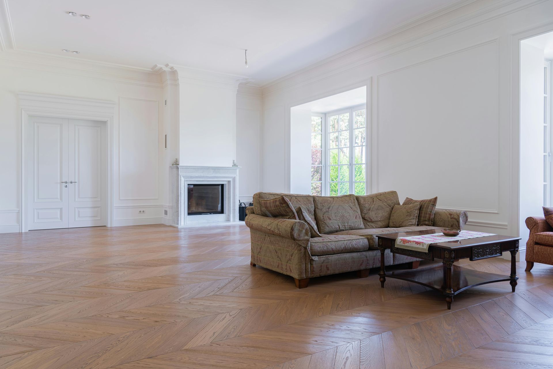 Bright empty living room with hardwood floors, white walls, fireplace, and a brown sofa with coffee table