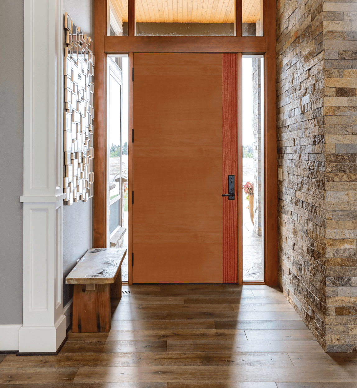 Front entry with an orange door, wood floor, stone wall, and bench in a bright hallway