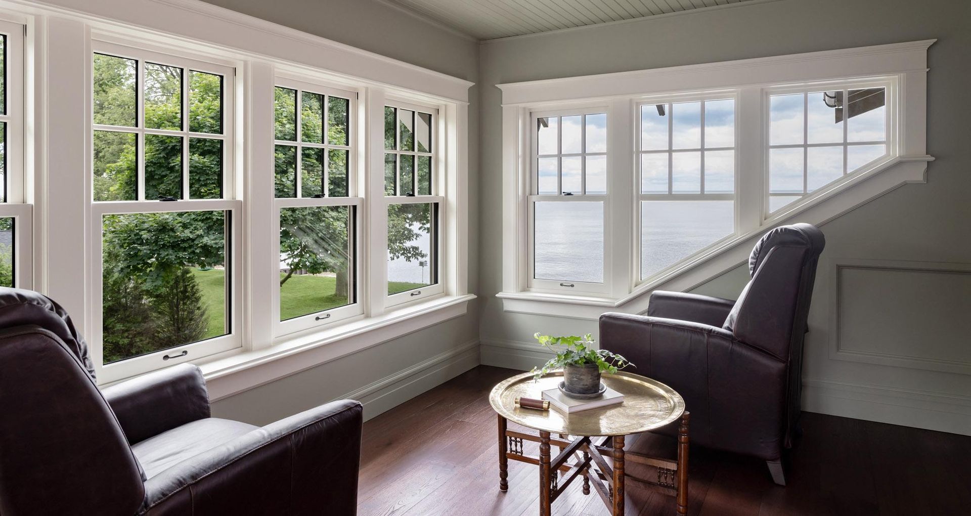 Bright living room with large windows, dark chairs, and a small round table by the corner window.