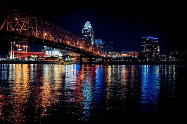 Night view of Cincinnati skyline with illuminated bridge reflected on the Ohio River.