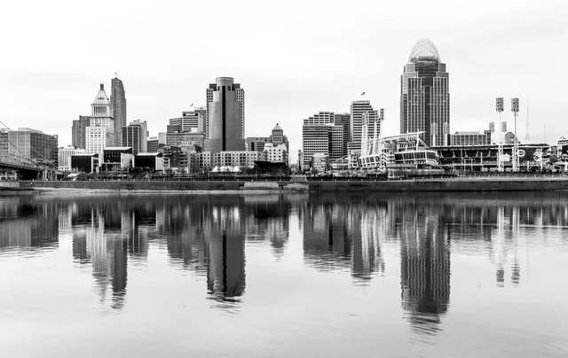 Cincinnati skyline reflecting in the river, monochrome. Buildings, stadiums, bridges against a cloudy sky.