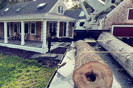a large log is sitting on the back of a truck in front of a house .