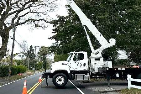 A white truck with a crane on the back is parked on the side of the road.