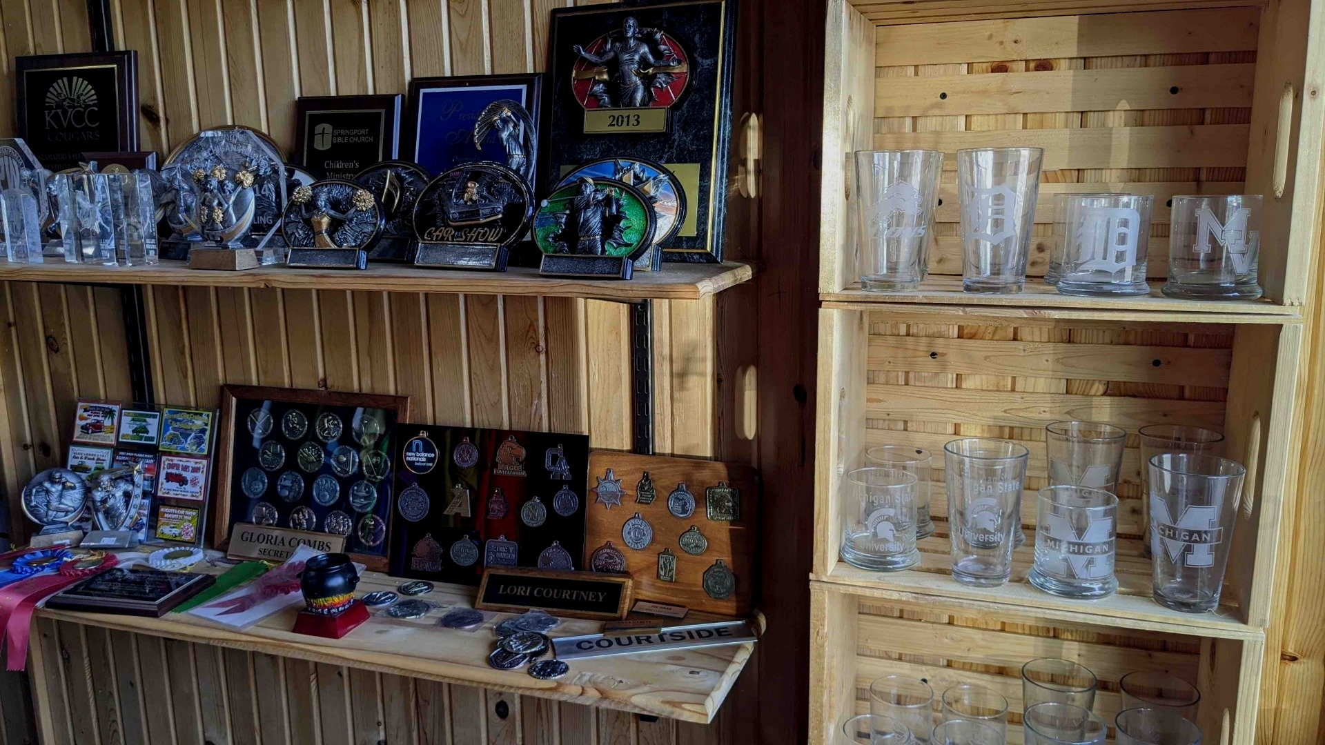 Wooden shelves displaying packaged souvenirs, decorative items, and rows of clear glass mugs