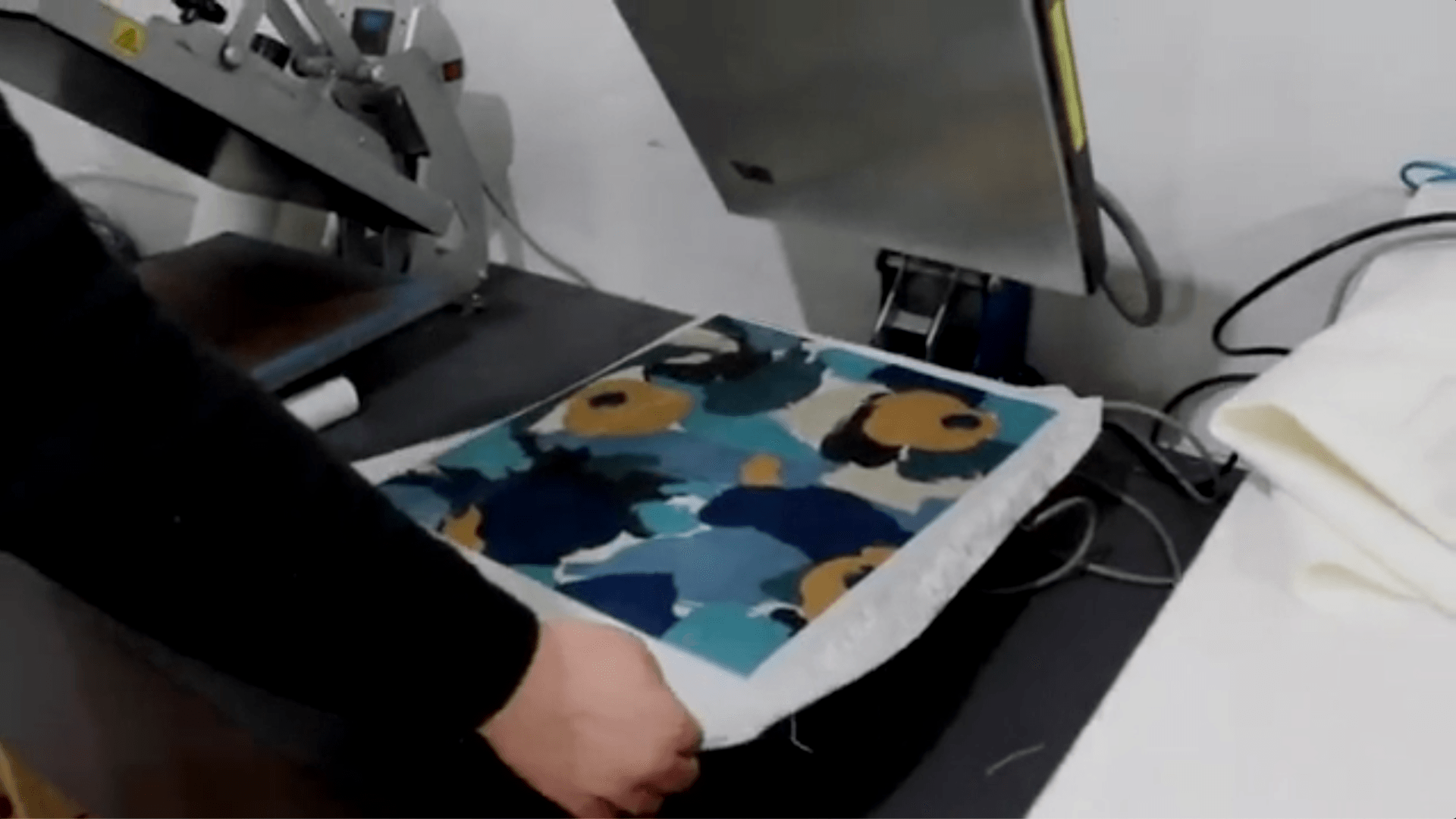Person loading a colorful printed fabric sheet into a machine in a workshop