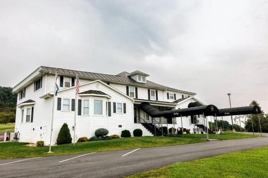Large white building with a black canopy over the entrance beside a paved road and grassy lawn
