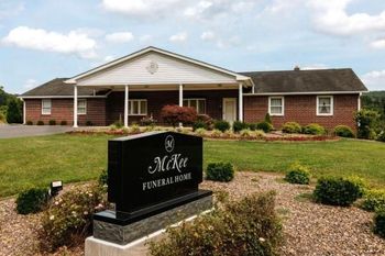 Brick funeral home with landscaped entrance and a black memorial sign in front.