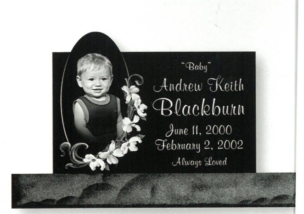 Black memorial plaque with oval child portrait, floral accents, and dates June 11, 2000–February 2, 2002