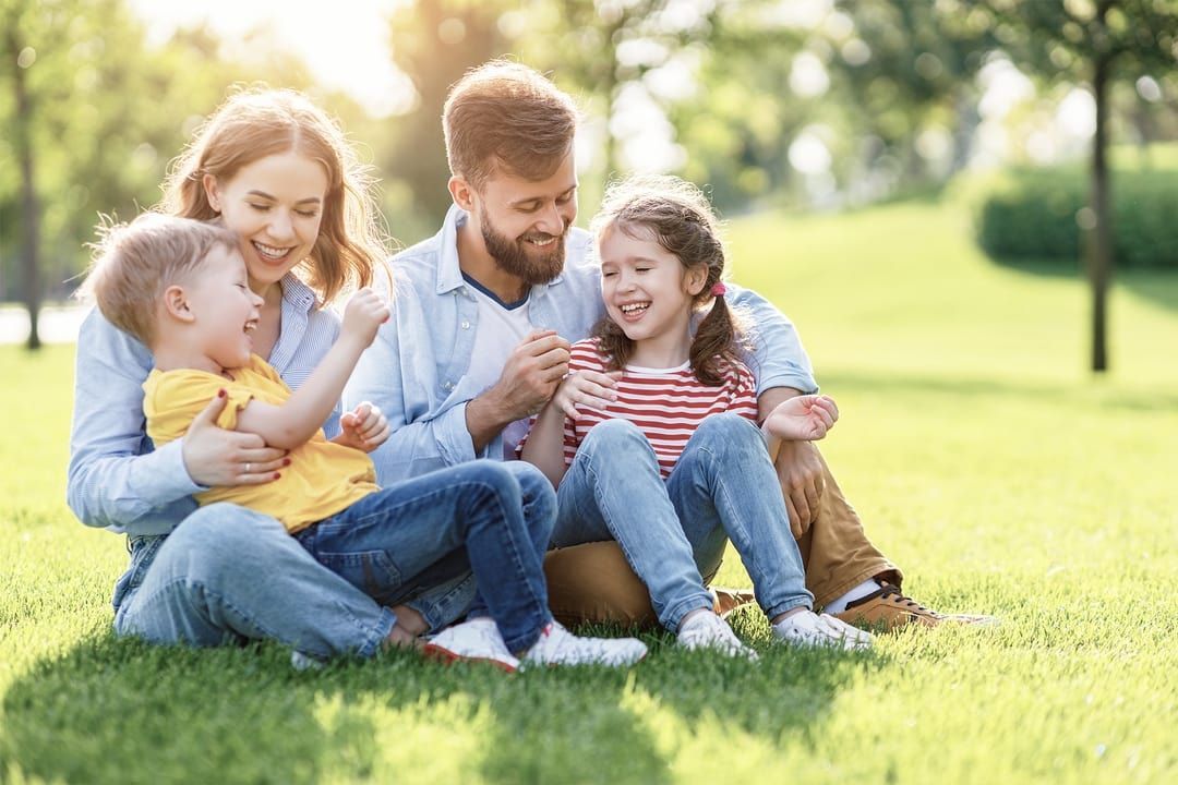 Family sitting on grass in a sunny park, laughing and playing together