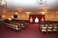 Empty banquet hall with rows of chairs, red carpet, patterned wallpaper, and chandeliers