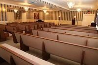 Empty church with rows of wooden pews and a stained-glass altar at the front
