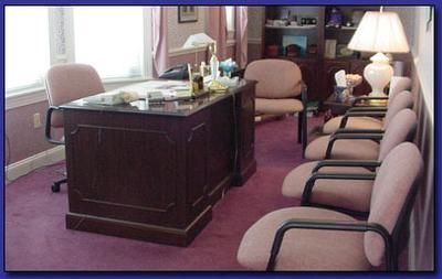 Conference room with a dark wooden desk, pink chairs, and a lit lamp near a window