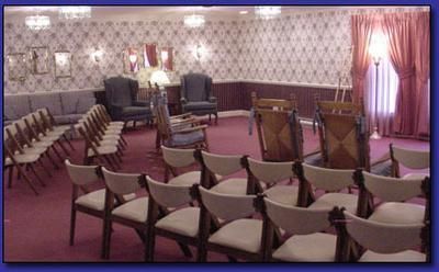 Empty auditorium with rows of chairs facing a podium and music stands on a patterned, mauve-carpeted stage