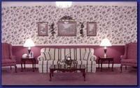 Pink living room with floral wallpaper, twin lamps, chairs, and a coffee table centered on a striped sofa.