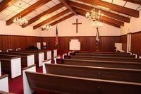 Wood-paneled church sanctuary with pews, altar, cross, and chandeliers under a vaulted ceiling