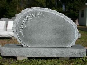 Gray oval gravestone with floral engraving on a stone base in a cemetery