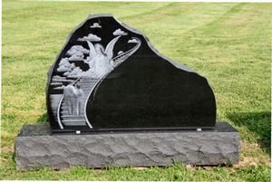 Black granite memorial headstone with engraved angel design on a stone base, set on grass