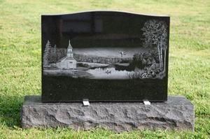 Black memorial stone with engraved landscape scene, set on a grassy lawn.