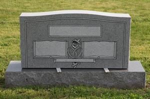 Gray granite grave marker with engraved panels and a central rose emblem on a grassy lawn