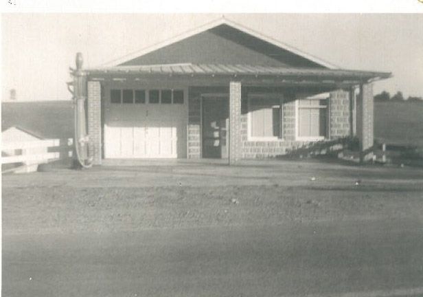 Black-and-white photo of a small house with a garage, front porch, and open yard.