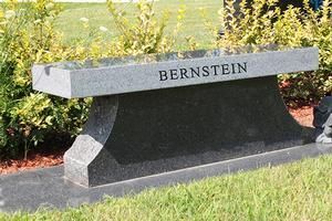 Gray granite memorial bench with the name “BERNSTEIN” in a grassy garden area