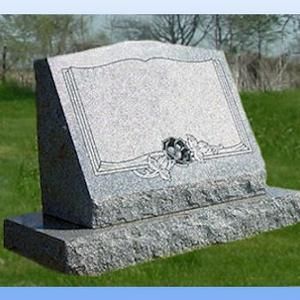 Gray granite gravestone monument with an engraved frame and floral wreath in a grassy cemetery