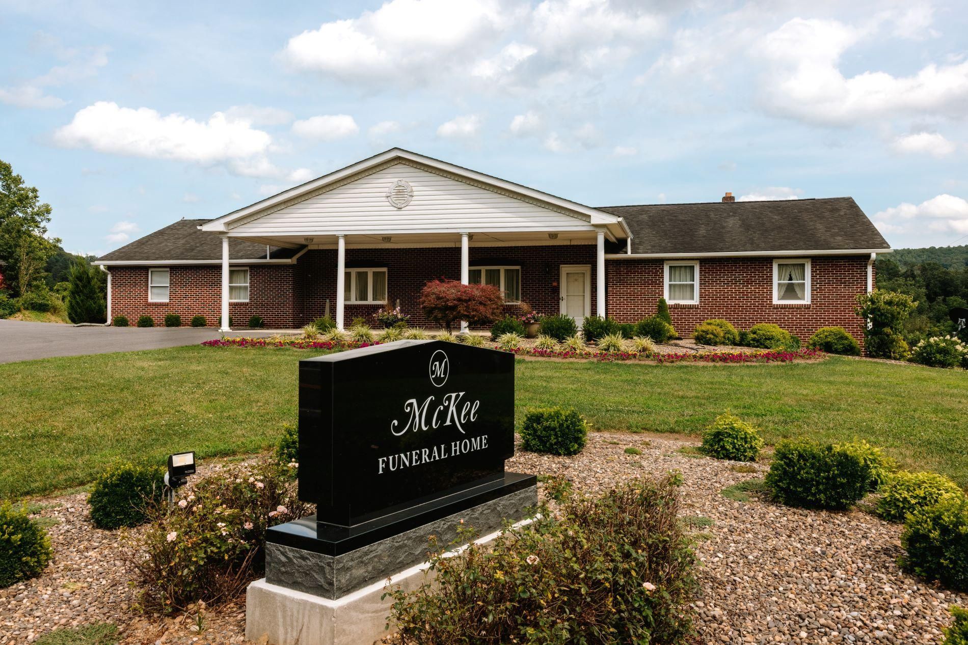 Brick funeral home with a white portico and sign in front, set in a landscaped lawn under a blue sky.