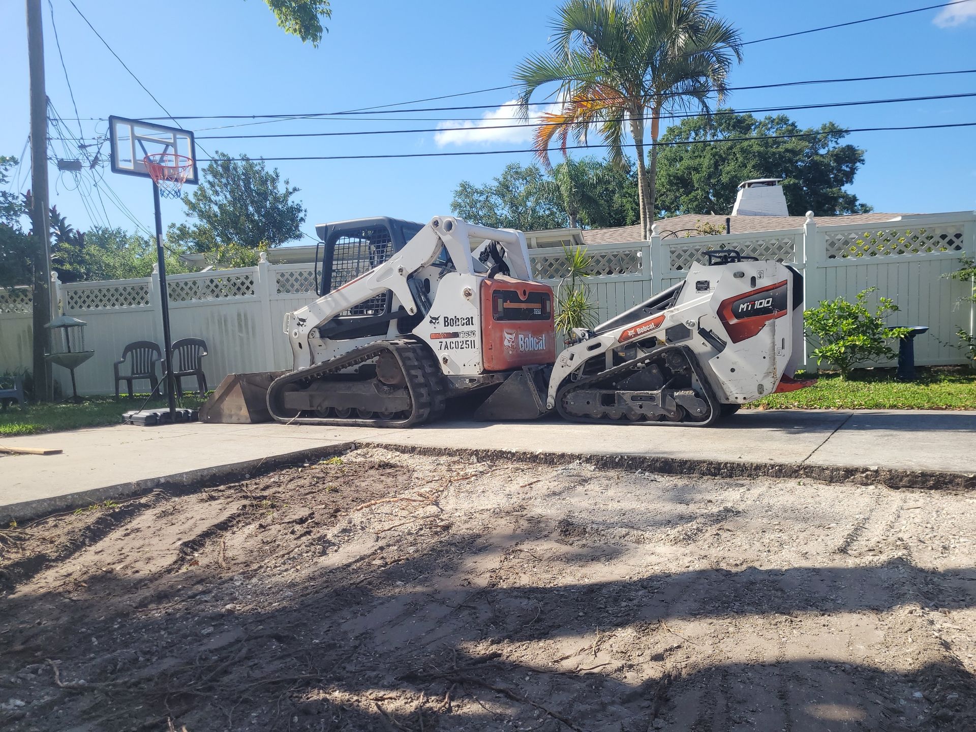 A Bobcat skid-steer loader at work demolishing pavement in a residential yard.