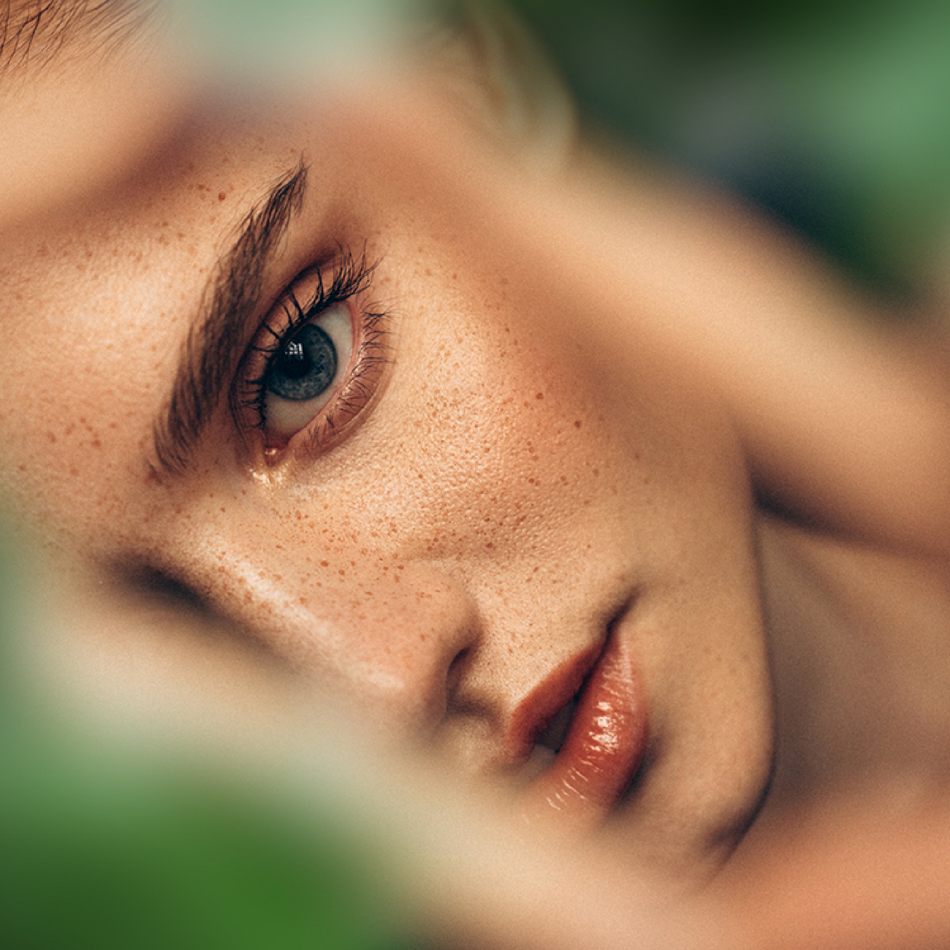 Eine Nahaufnahme des Gesichts einer Frau mit Sommersprossen vor grünem Hintergrund.