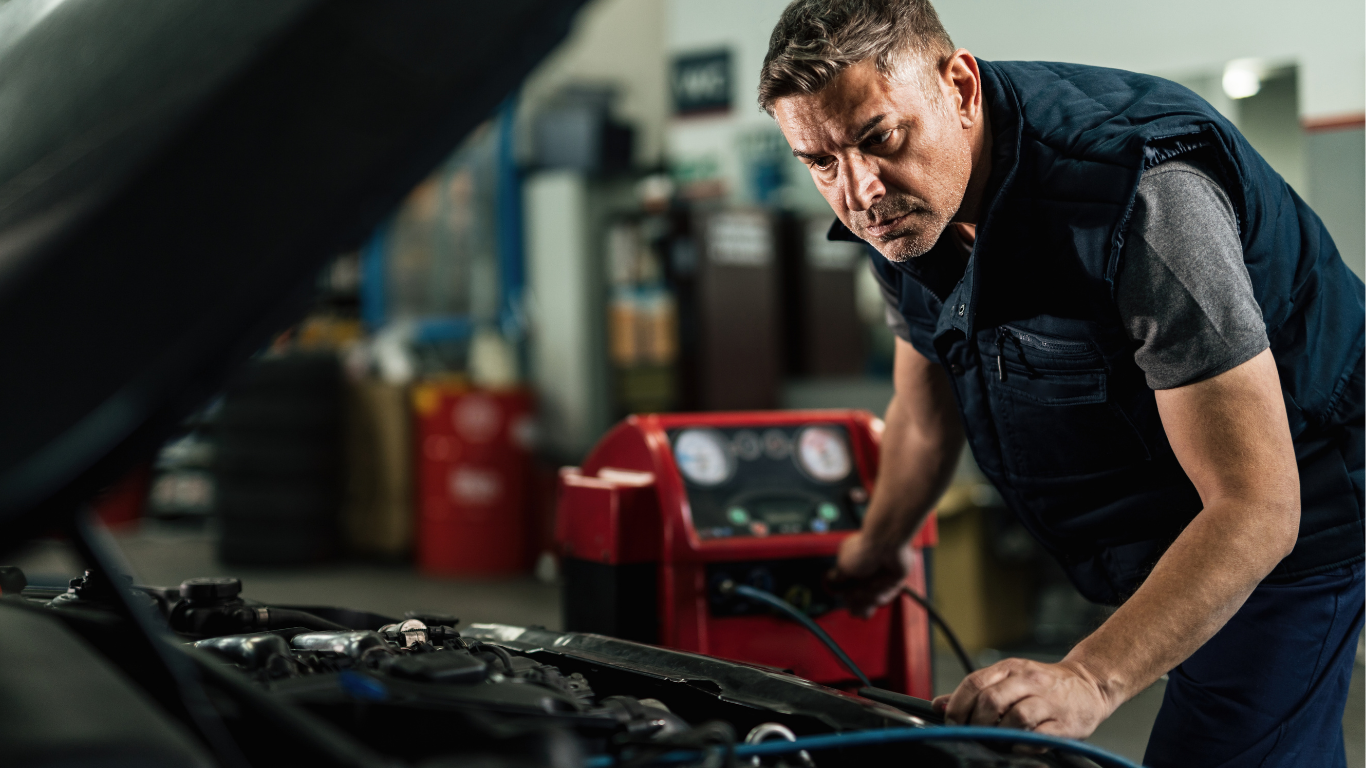 Mechanic inspecting a car engine in an auto repair shop, leaning over the open hood.
