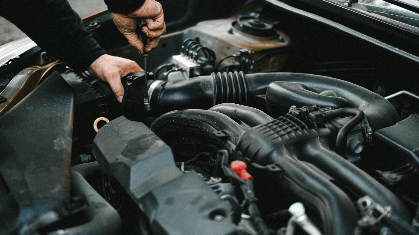 Hands inspecting a car engine compartment with black hoses and components.