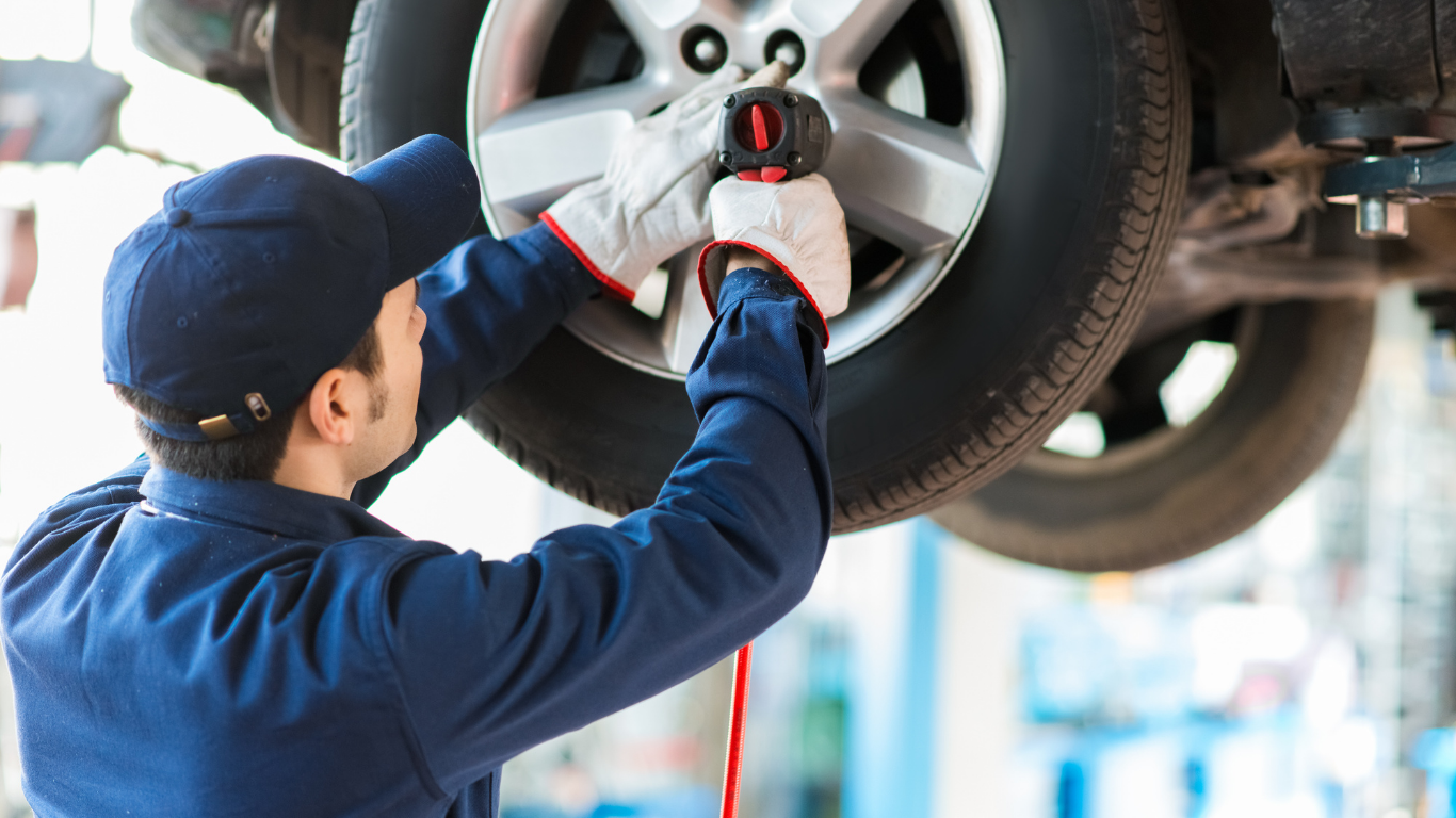 Mechanic in blue uniform using a wrench to change a car tire on a lift
