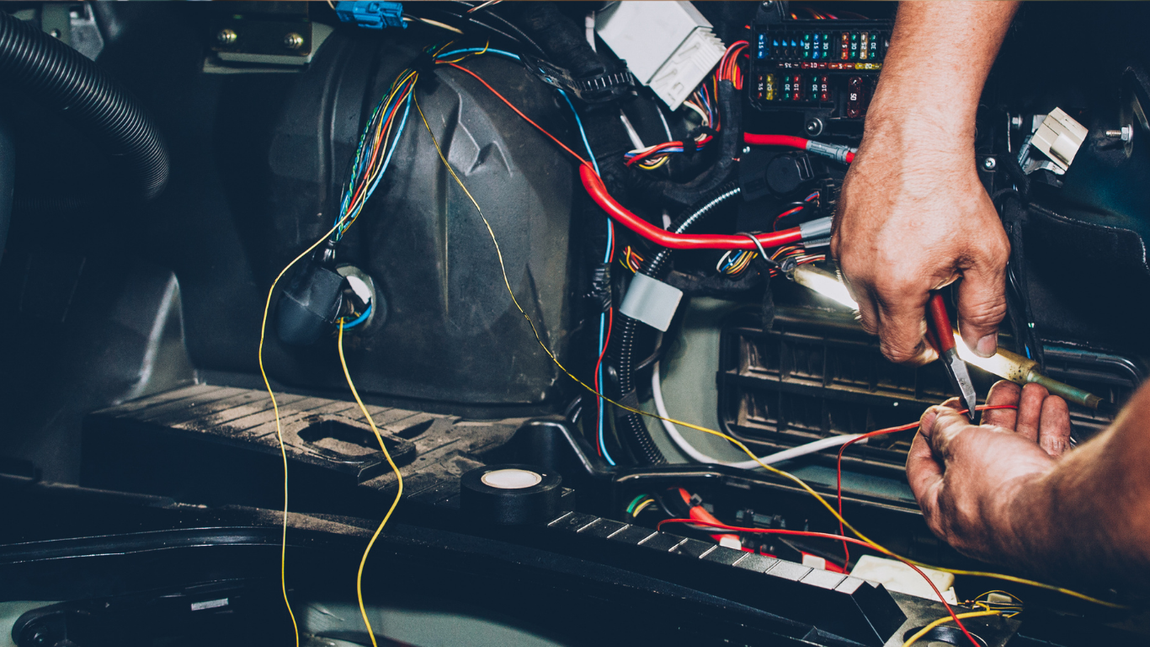 Hands repairing car wiring and dashboard electronics inside a vehicle interior.