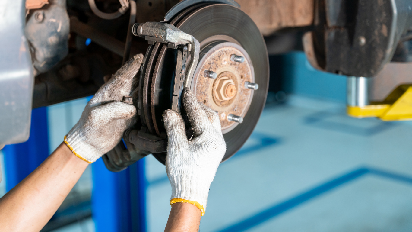 Mechanic wearing gloves installs brake pads on a car’s wheel hub in a garage.