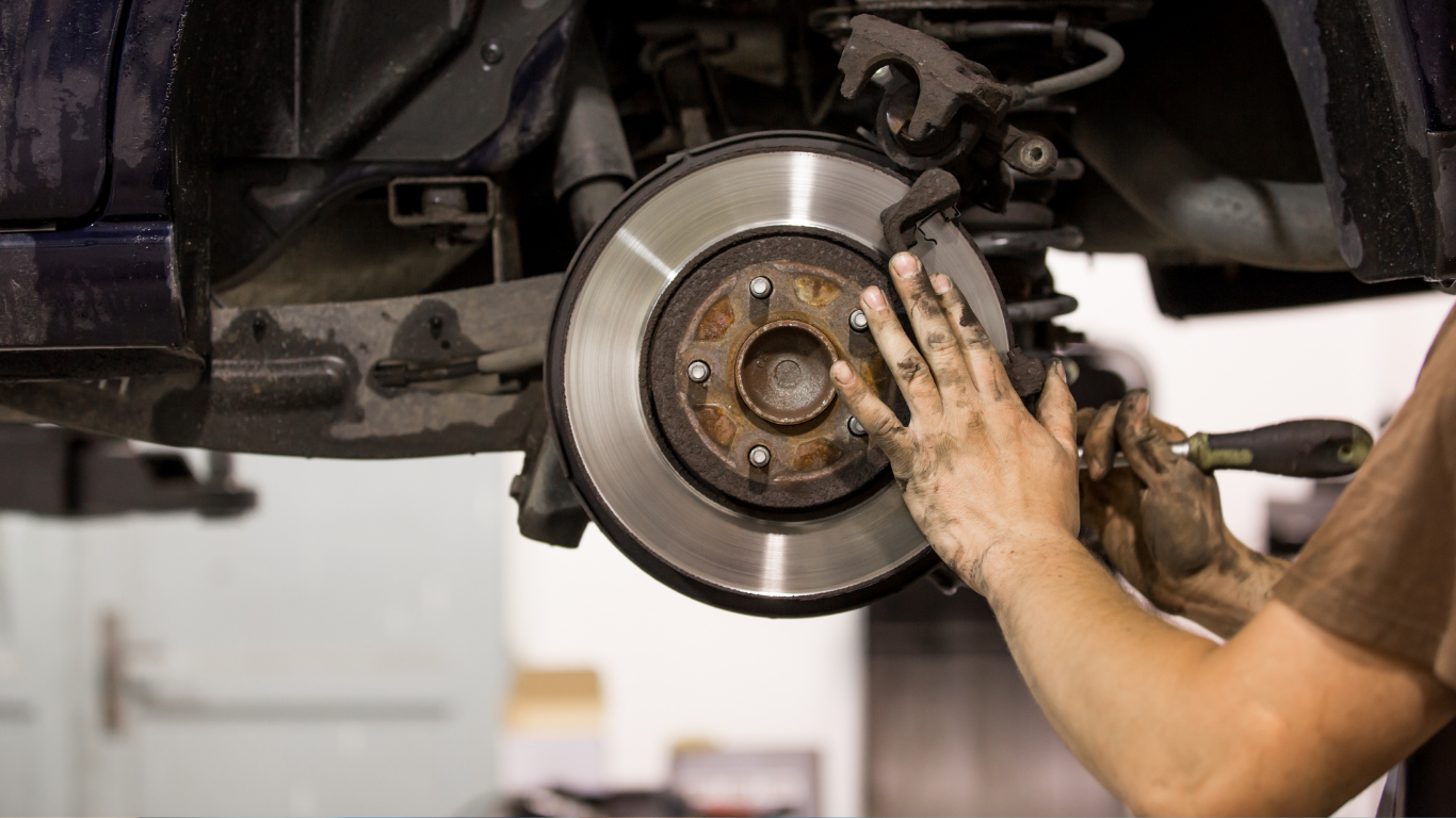 Mechanic working on a car’s exposed brake rotor and wheel hub in a garage