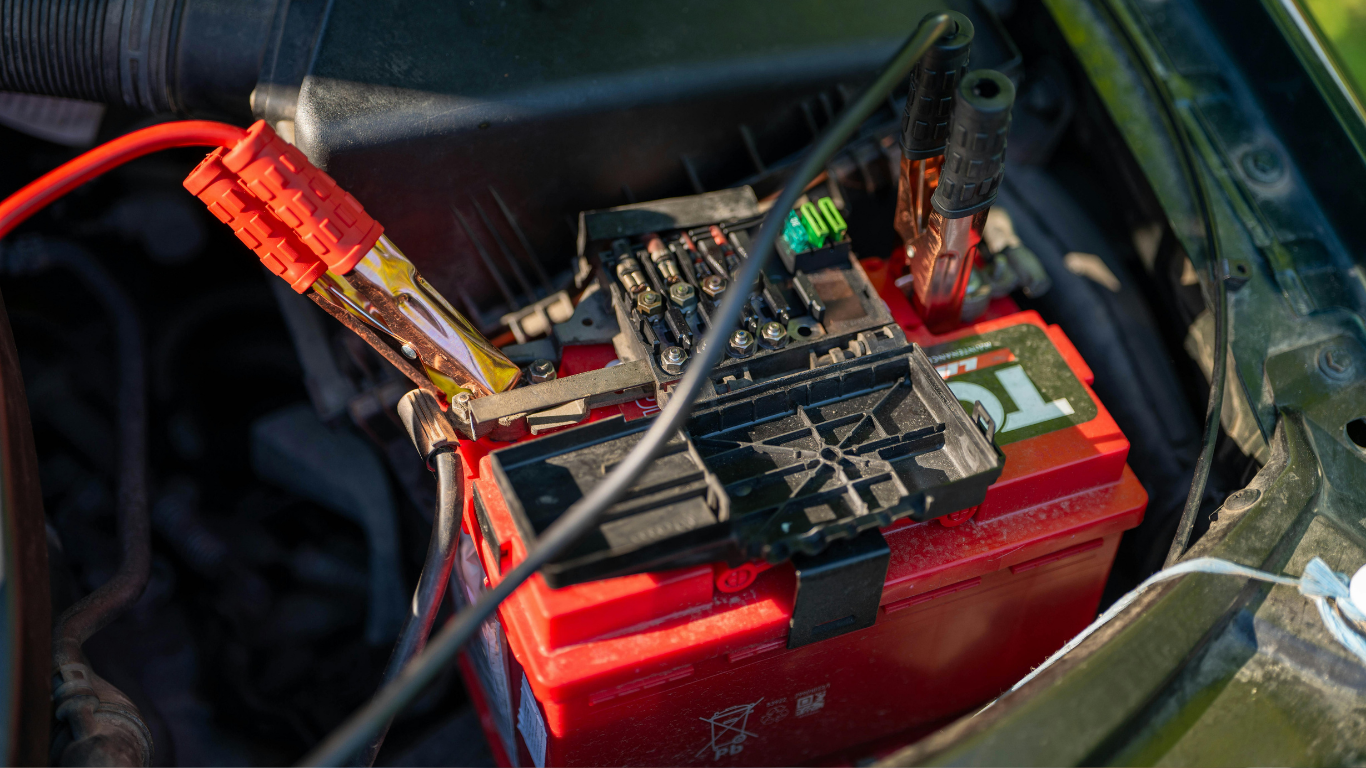 Red battery with a circuit board and wires attached inside a vehicle compartment