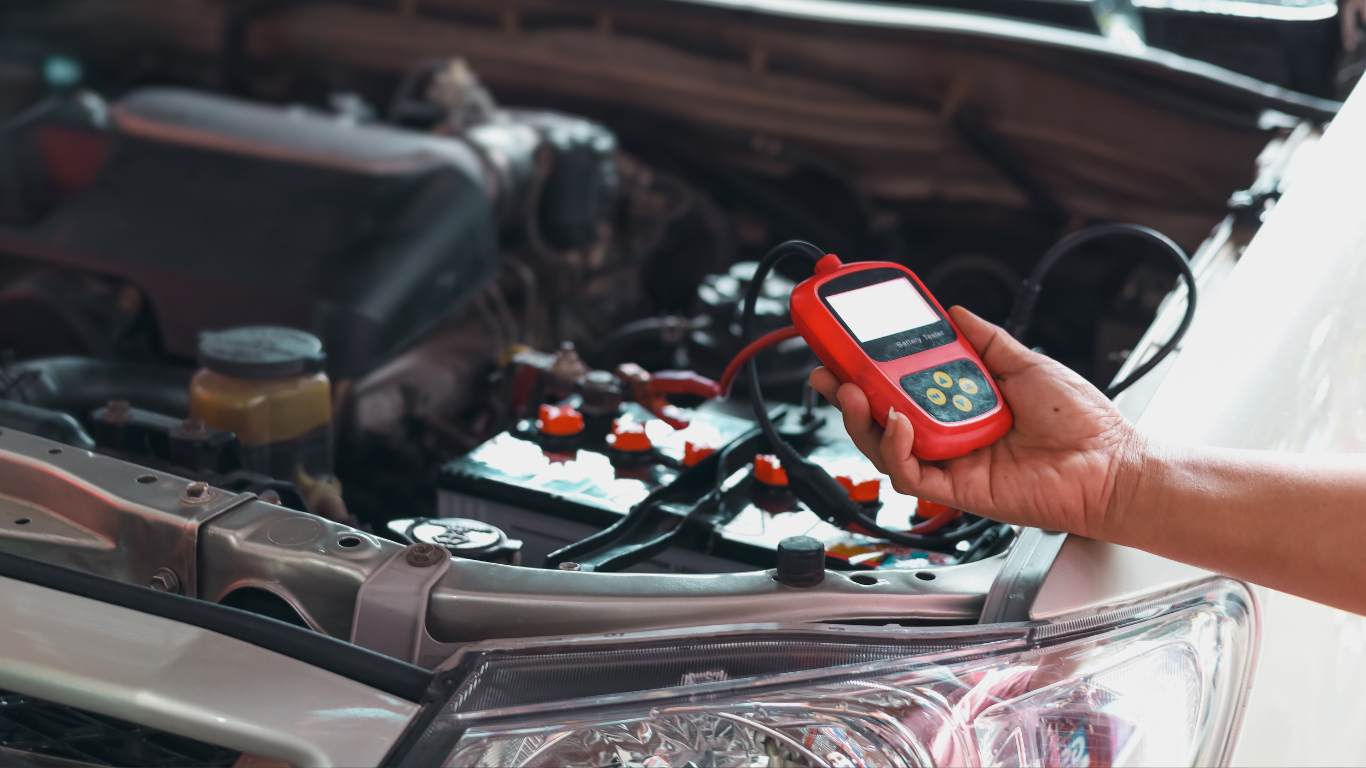 Mechanic using a red car battery tester on a car engine in the open hood