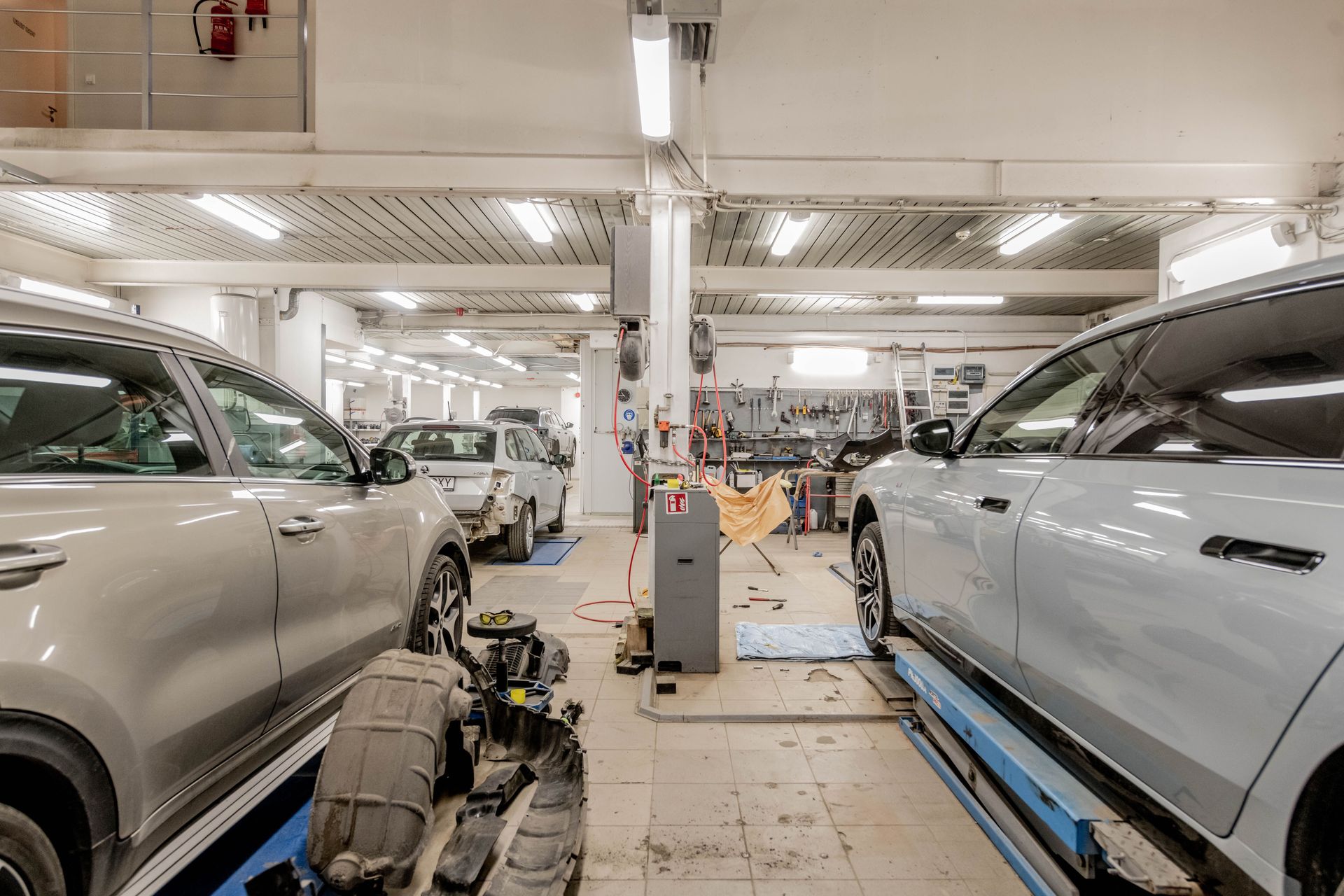 Car service bay with two silver SUVs and mechanics working under bright lights