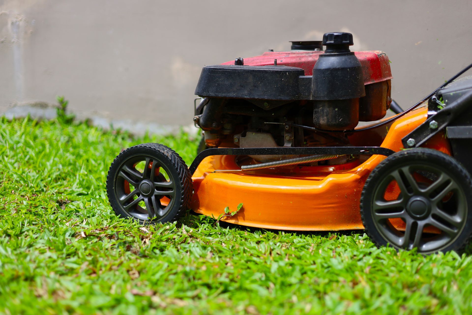 Orange lawn mower on green grass near a wall.