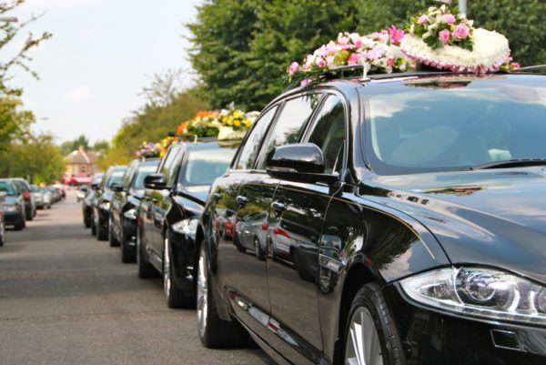 A row of black cars with flowers on top of them are parked on a street.