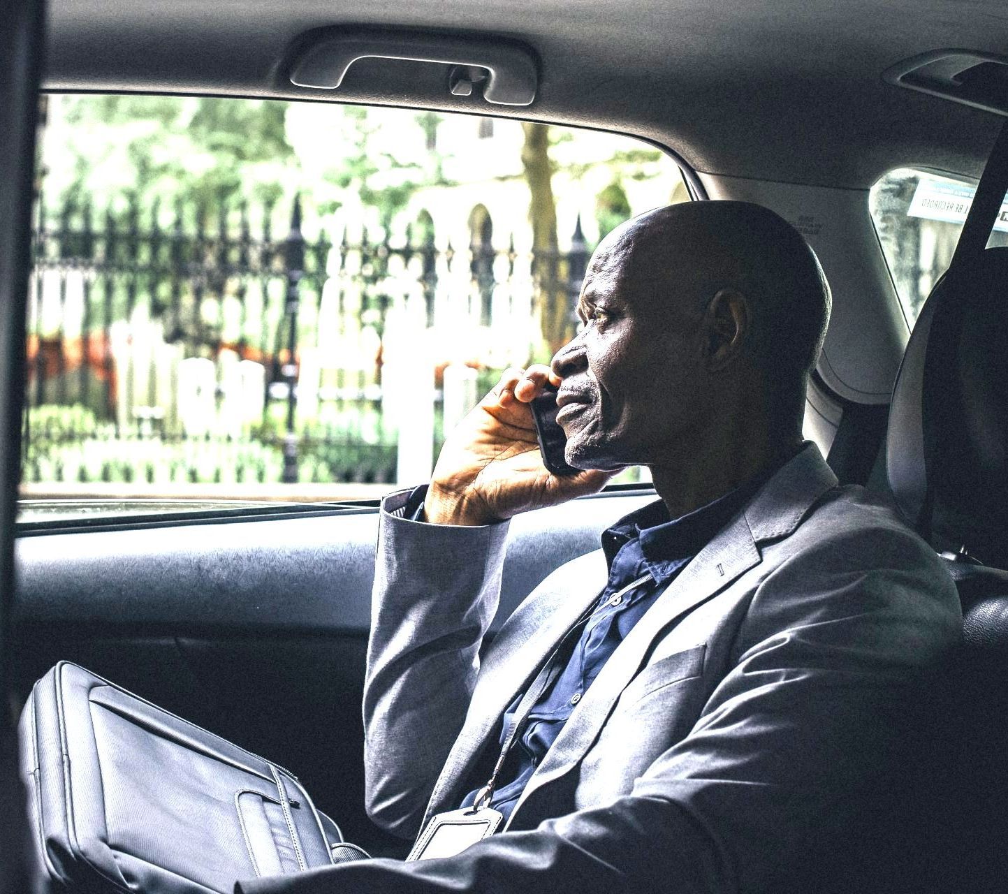 A man in a suit is sitting in the back seat of a car talking on a cell phone