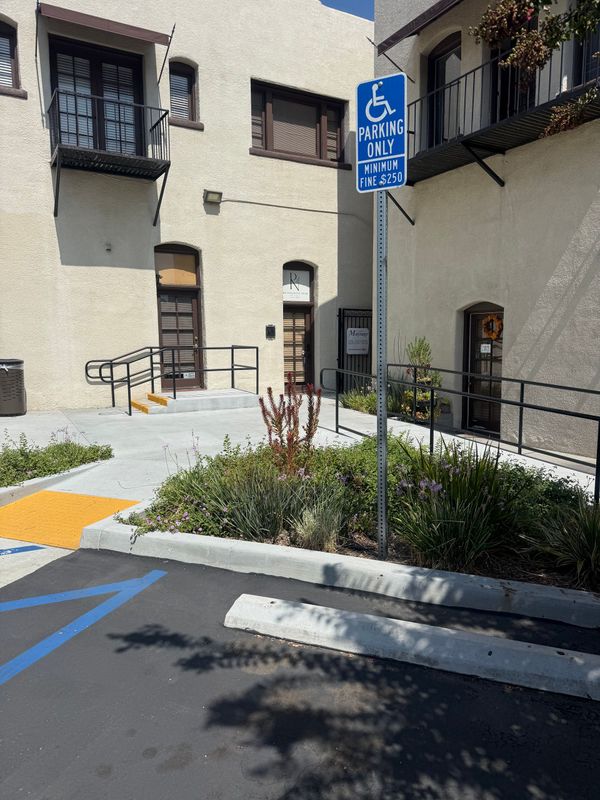 Accessible parking sign beside a ramp and curb cut in front of a beige building