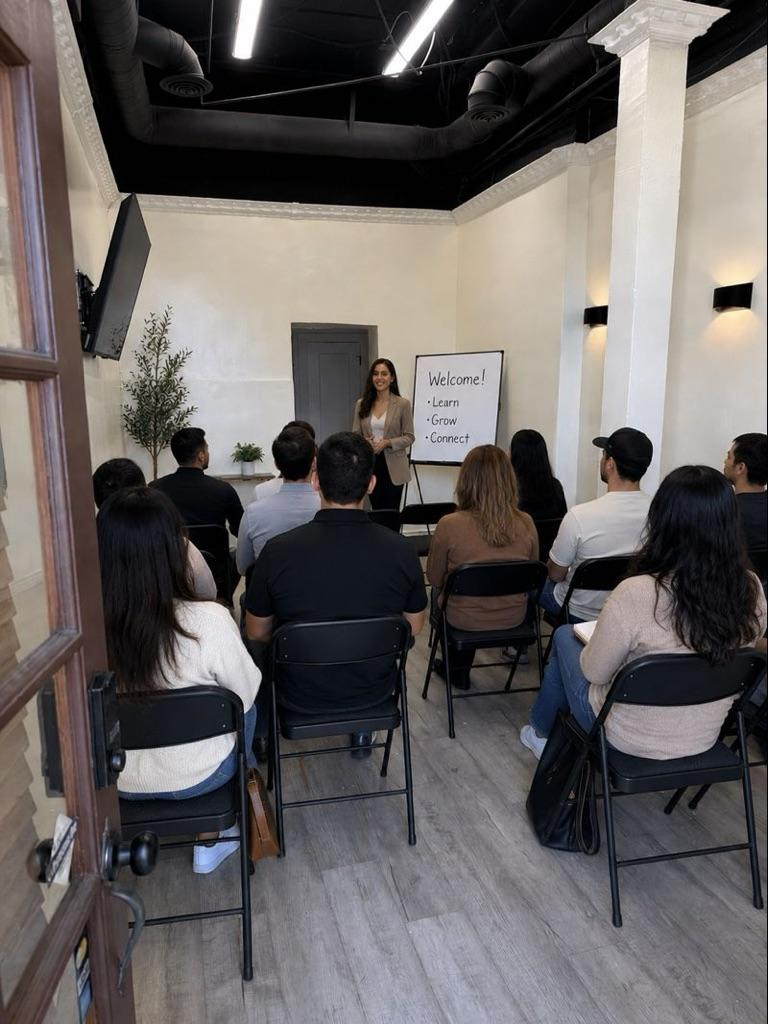 Audience seated in a small white-walled room watching a presentation at the front