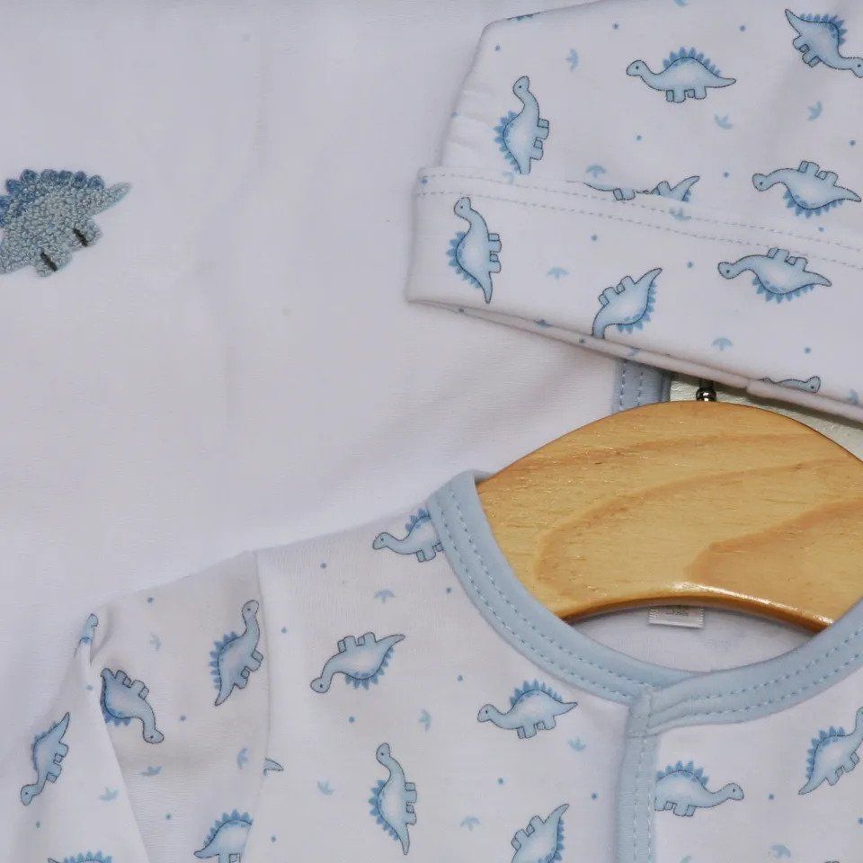 A white shirt with blue dinosaurs on it is hanging on a wooden hanger