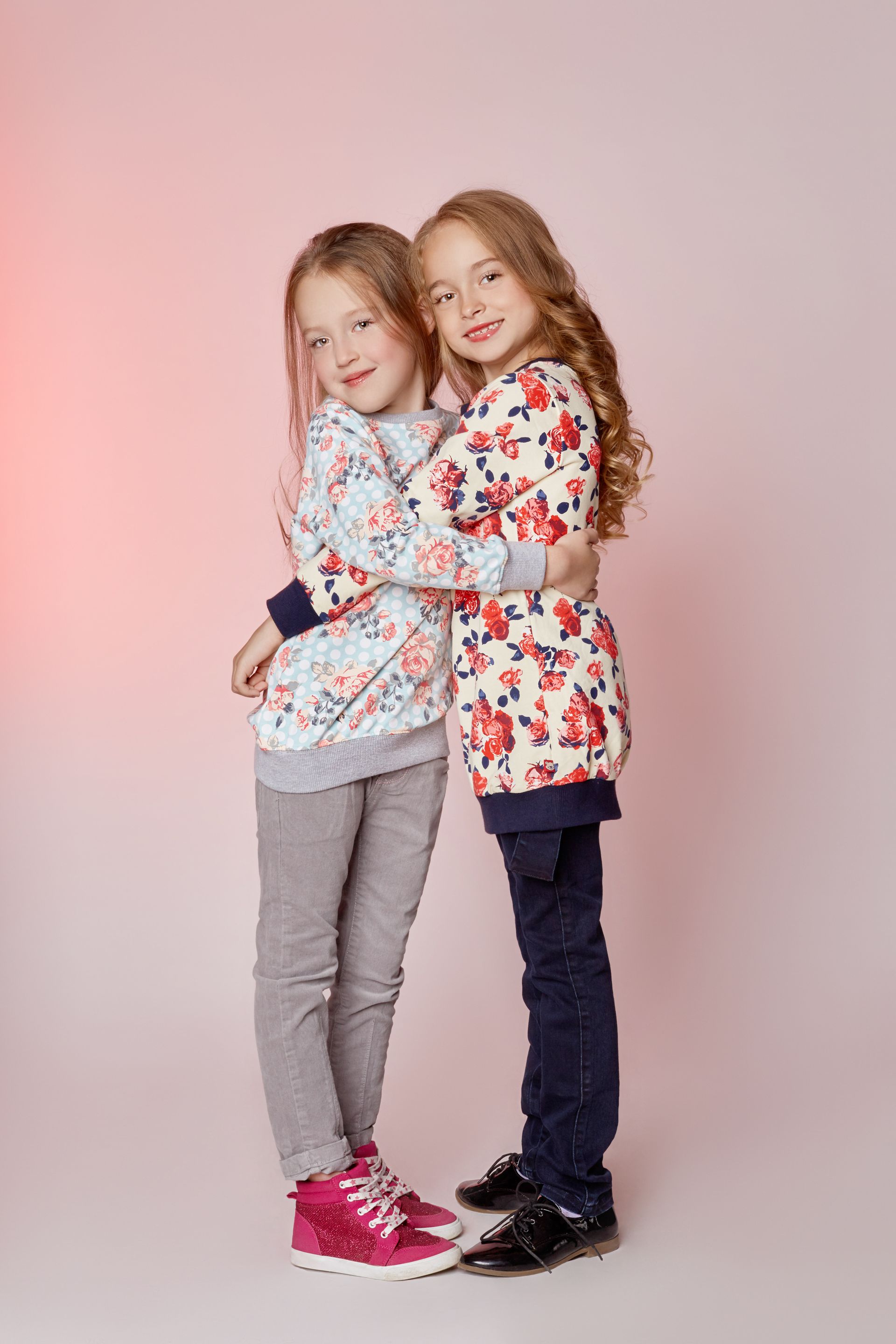 Two little girls are hugging each other on a pink background.