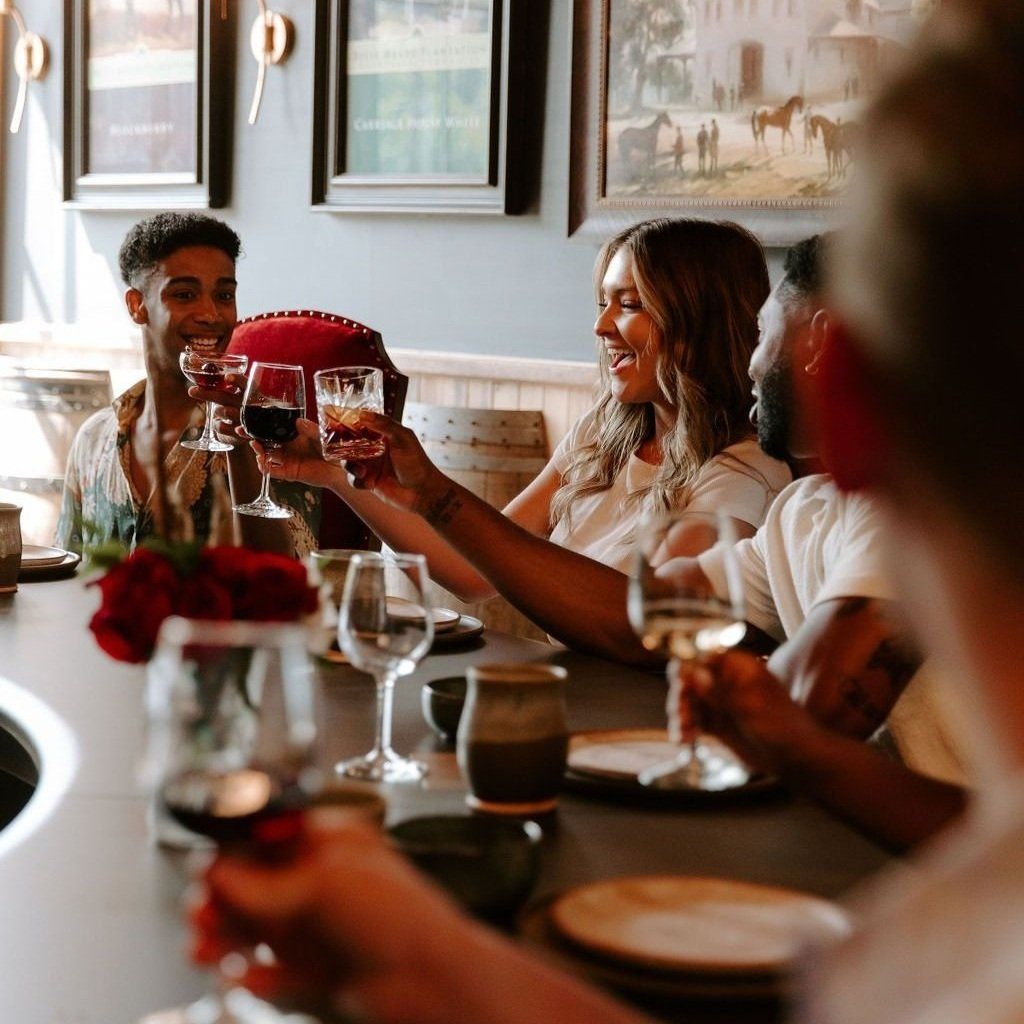 People toasting wine glasses in a restaurant. Smiling faces, wooden table, and artwork on the walls.