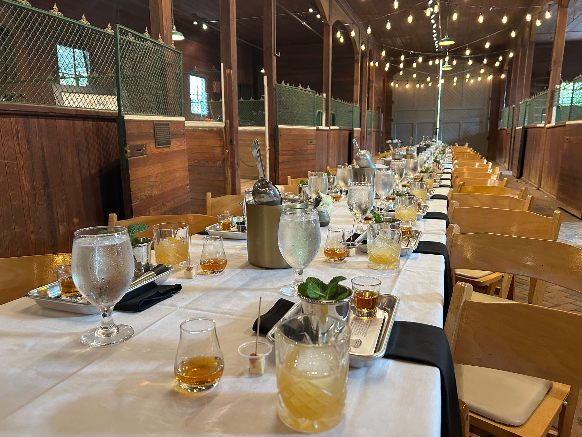 Long table set for a dinner in a rustic wooden stables, with drinks and decor.