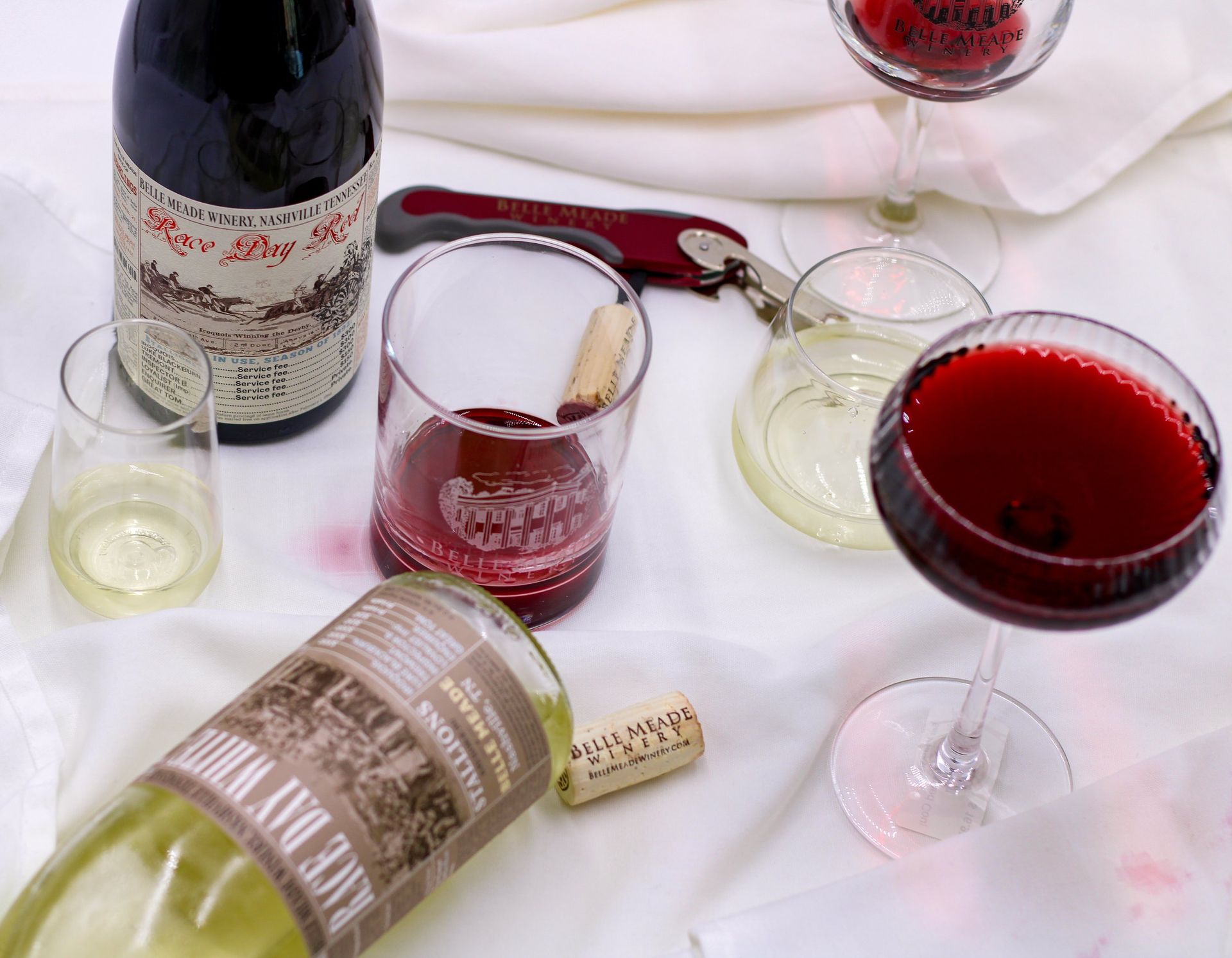 Wine glasses and bottles on white cloth, corkscrew, red and white wine, a festive setting.