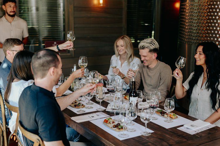 People toasting with wine glasses at a wooden table in a winery.