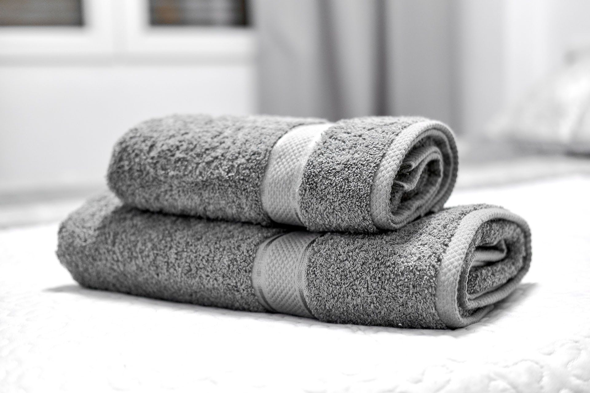 Two gray towels are stacked on top of each other on a bed.